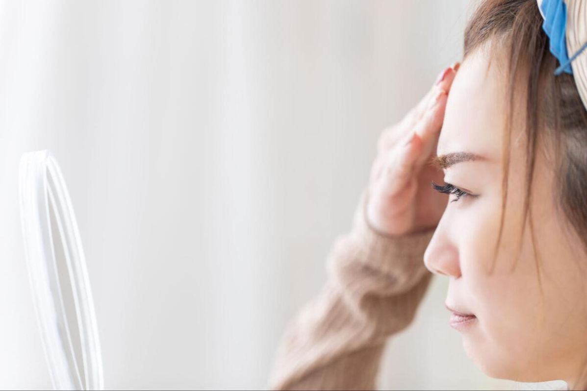 鏡でおでこのシミの種類を確認する女性