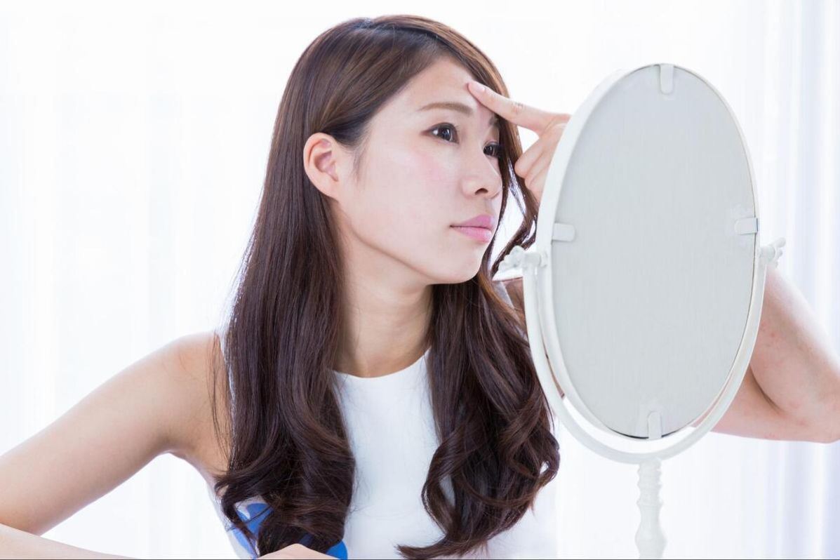 鏡でおでこを確認しながら人差し指で触る女性