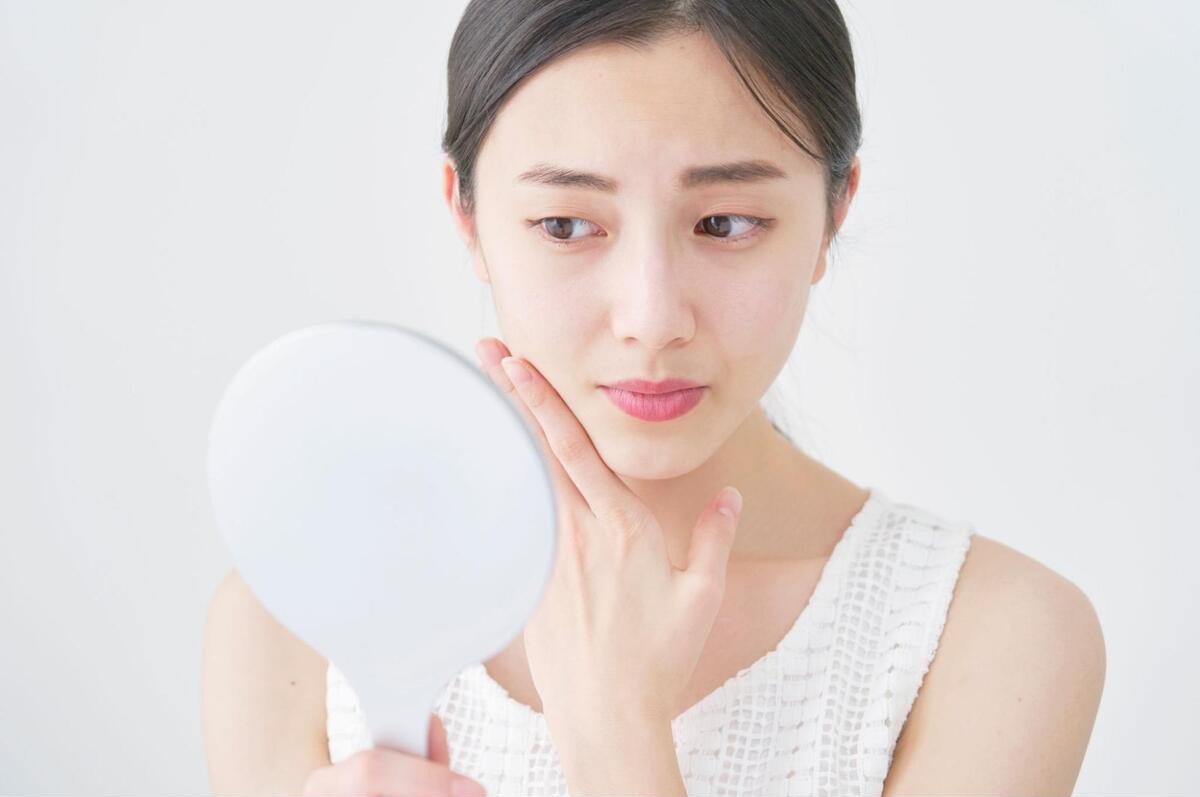 鏡を使用して顔の赤みを確認する女性