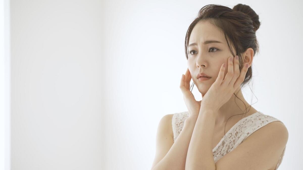 赤ら顔の原因を確認するために両手で頬を触れる女性