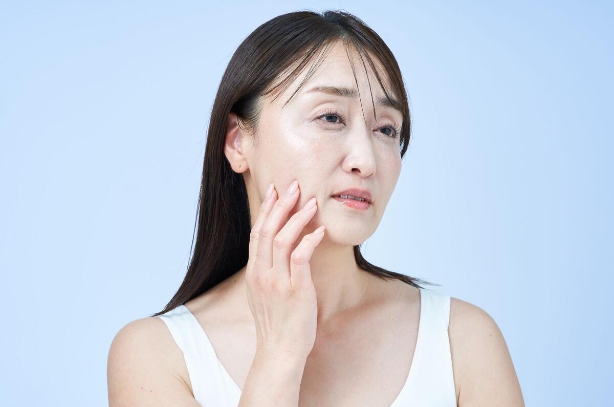 顔のたるみを気にして顎あたりの肌を手で触れている女性