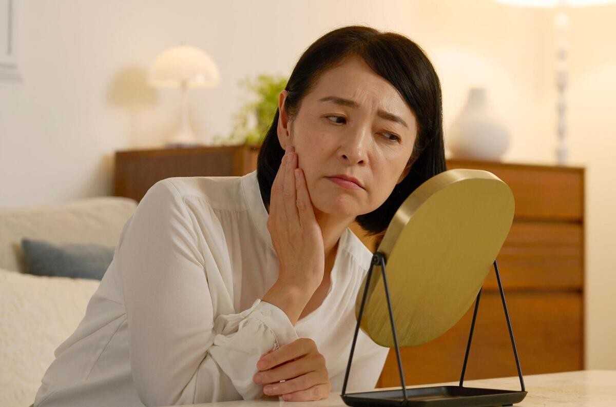 鏡を見て顔のたるみを確認する女性